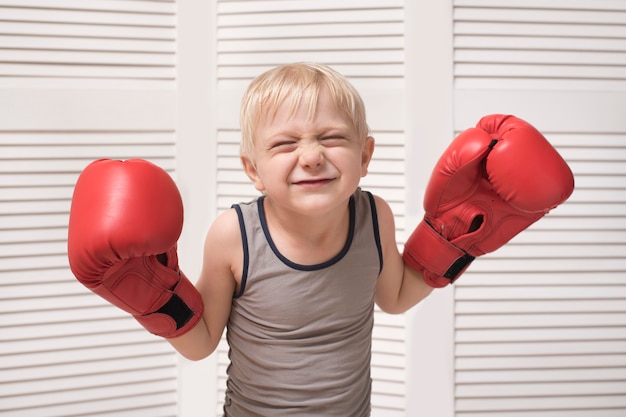 Funny blond boy in red boxing gloves. Sports concept