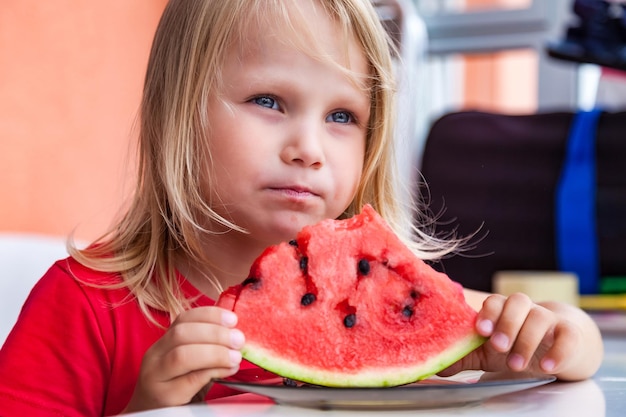 Funny blond child portrait with watermelon indoors looking away pretty little toddler girl 4 year eating watermelon