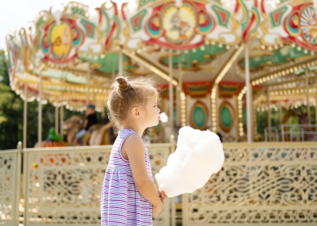Funny blonde girl in colorful dress eating cotton candy at the carnival