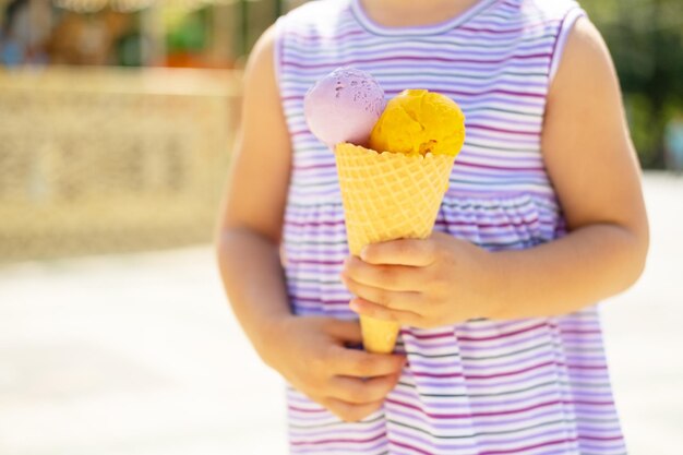 Funny blonde girl in colorful dress eating ice cream in waffle cone Summer food