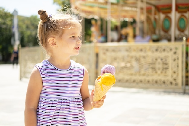 Funny blonde girl in colorful dress eating ice cream in waffle cone Summer food