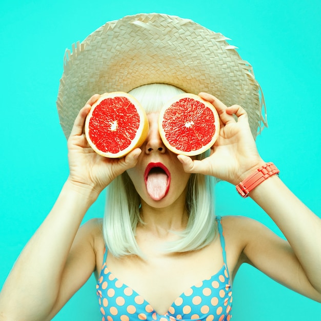 Photo funny blonde in swimsuit polka dot on a blue batskground with grapefruit. retro summer style