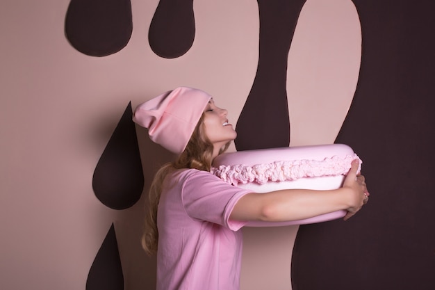 Смешная белокурая женщина в розовой футболке и кепке развлекается с большим миндальным пирогом. Концепция праздника