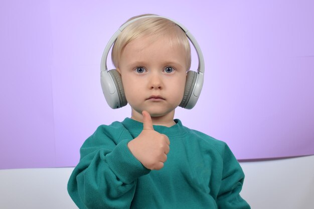 Funny boy child listens to music in headphones and shows thumbs up