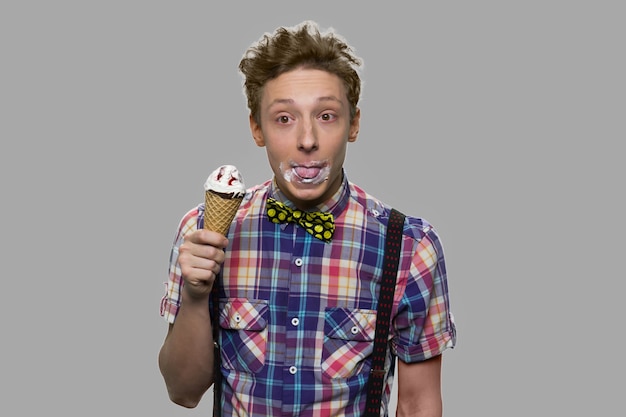 Funny boy eating an ice cream close up. Cute teenage guy enjoying of delicious ice cream on gray background. Carefree childhood concept.