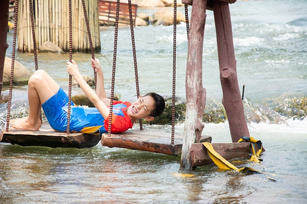 Funny boy enjoy playing swinging in canal at countryside of Thailand