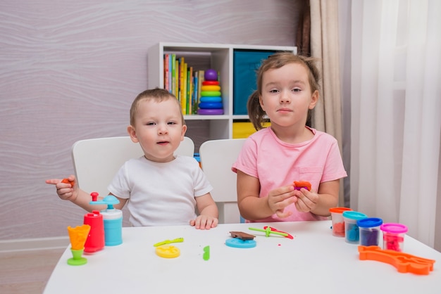 Funny boy and girl play play-doh at the table in the children's room