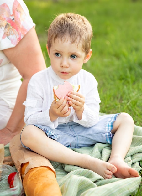 ピクニックを持つ面白い少年。クックアウトでサンドイッチを食べる小さな子供