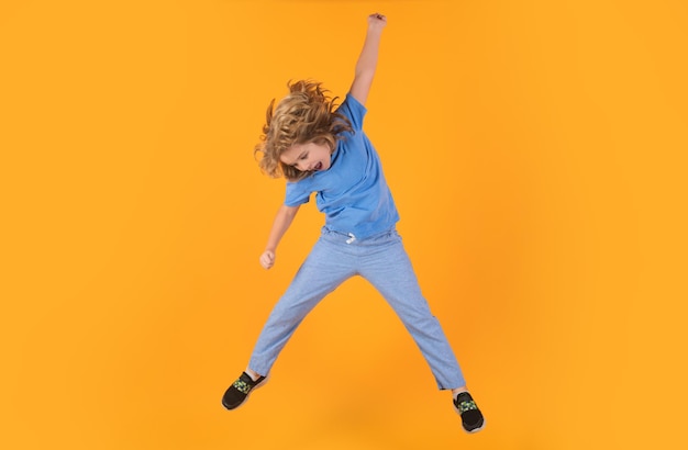 Funny boy jumping energetic kid boy jumping and raising hands up on isolated studio background full length body size photo of jumping high child boy hurrying up running fast on yellow background