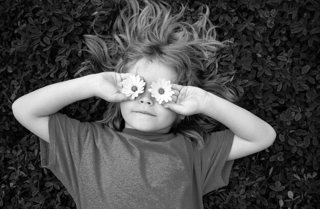 Foto funny boy kid en daisies gelukkige kleine blonde haar kind met bloemen ogen liggen op het gras met daisies bloemen kind dromen en glimlachen tegen kamille veld