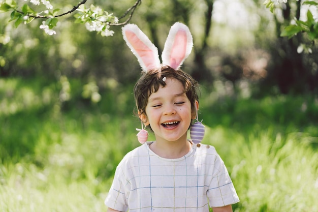 Funny boy with eggs basket and bunny ears on easter egg hunt in sunny spring garden