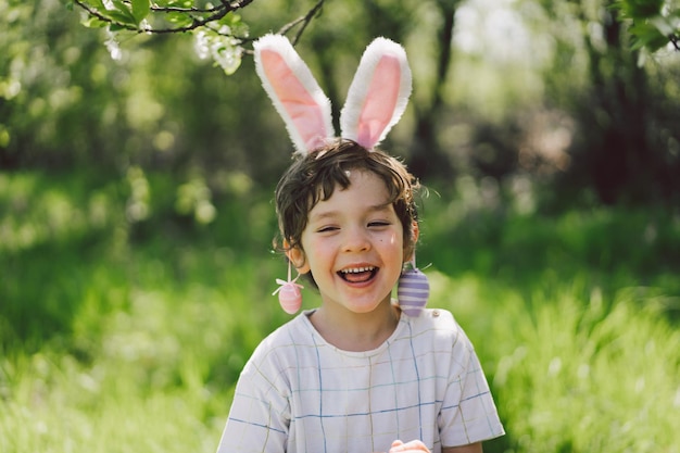 Funny boy with eggs basket and bunny ears on easter egg hunt in sunny spring garden