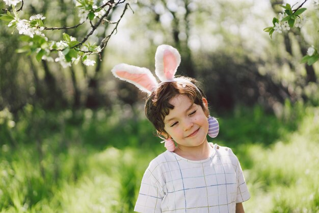 Funny boy with eggs basket and bunny ears on easter egg hunt in sunny spring garden