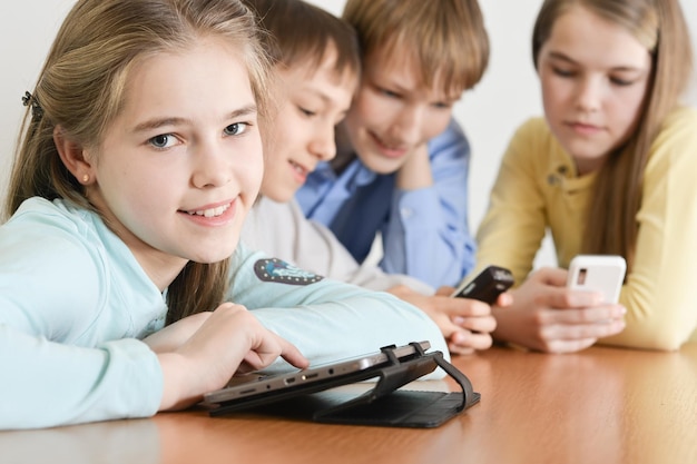 Funny boys and girls using digital devices together at the table at home