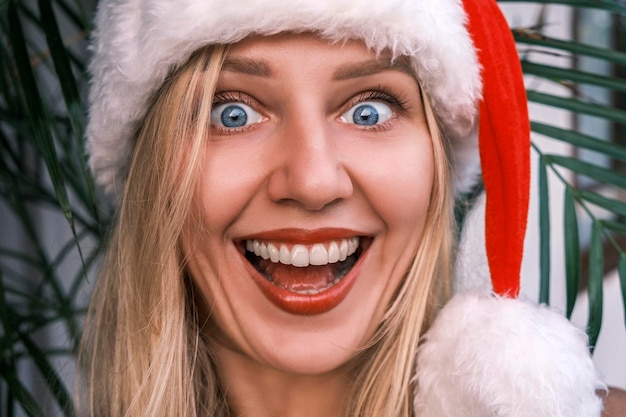 Foto divertente donna bionda sorridente che indossa il cappello della santa che esamina la macchina fotografica con gli occhi sorpresi ragazza celeb