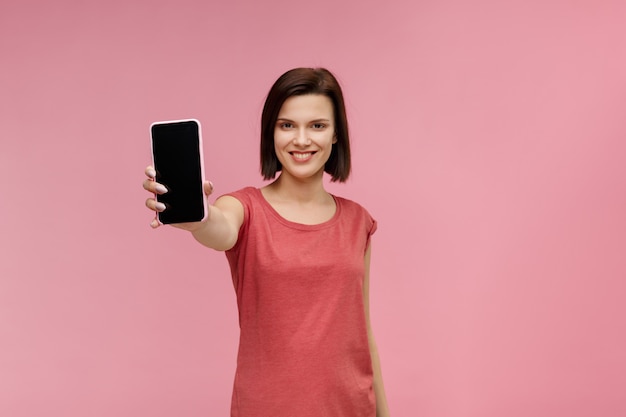 Funny brunette woman showing blank screen mobile phone on camera.