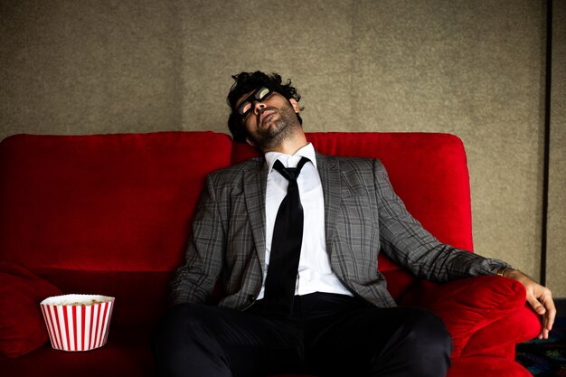 Funny business man watching movie with popcorn on red sofa