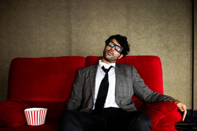 Funny business man watching movie with popcorn on red sofa