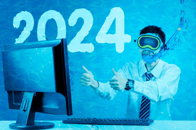 Funny businessman underwater showing thumbs up on the computer monitor with the 2024 new year numbers