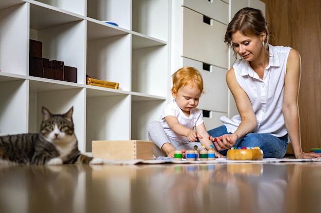 おかしい猫のリラックスしたお母さんと小さな幼児が一緒に遊んでいる子モンテッソーリ法の自己学習