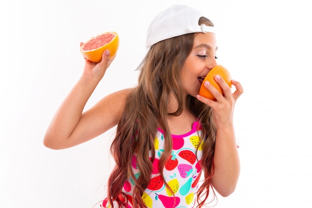 A funny caucasian girl with long hair, swimsuit, white cap holds grapefruit halves and smells them