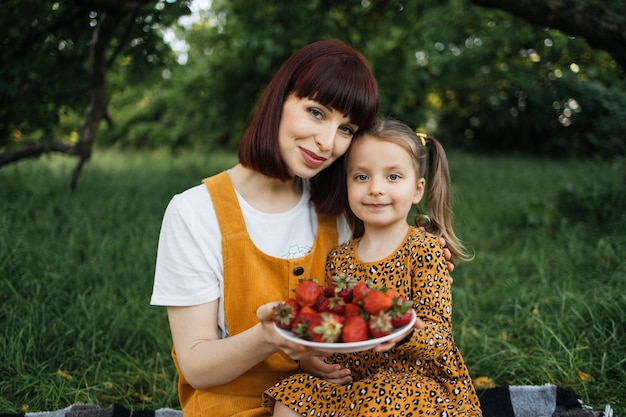 Funny caucasian mom and daughter at the picnic eating strawberry