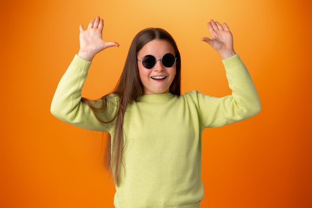 オレンジ色の背景に分離された眼鏡の面白い白人の十代の少女