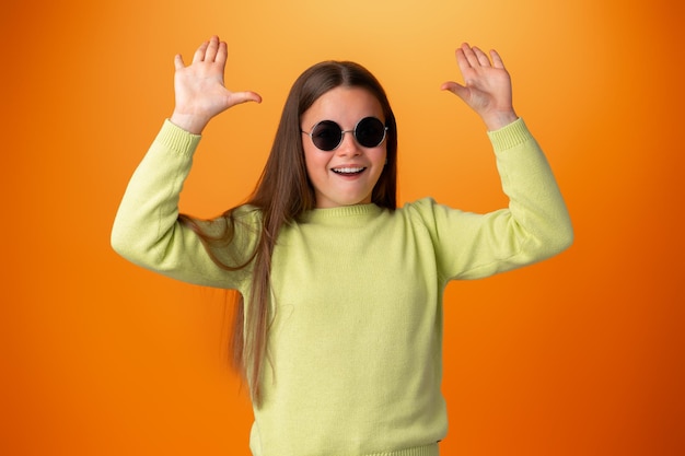 Funny caucasian teen girl in eyeglasses isolated on orange background