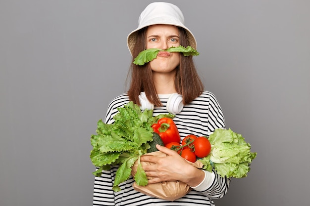 Photo funny caucasian woman holding organic vegetables standing isolated over gray background making mustache with green lettuce looking at camera