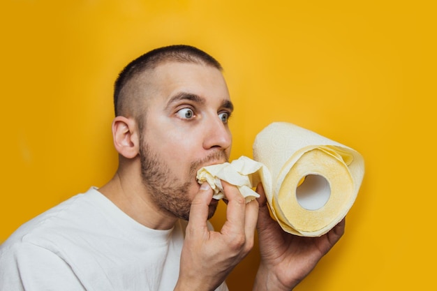 Funny caucasian young man eats a toilet paper He forgot to buy food in coronavirus panic Studio shot