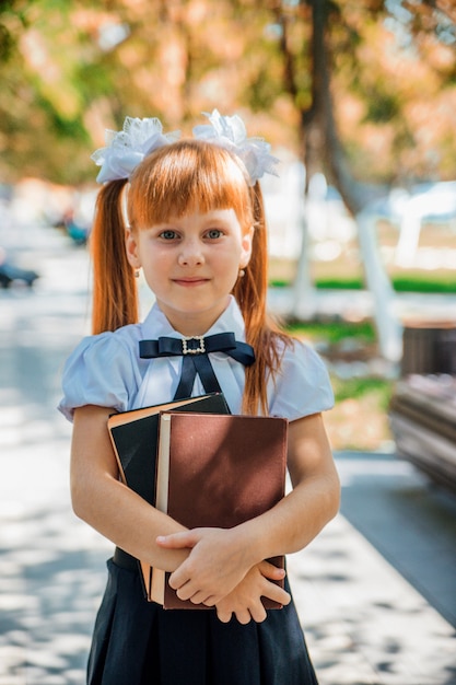 学校や幼稚園の初日に、本を手にした面白い魅力的な少女。子供は暖かい晴れた日に外にいます、コンセプトは学校に戻っています。