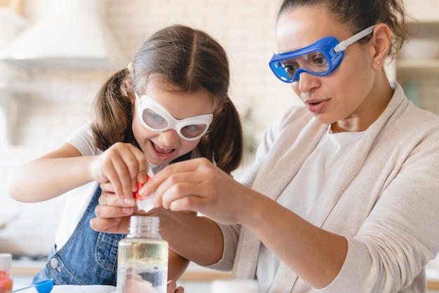 Funny chemistry Closeup cropped scientific experiment at home Laboratory tests for school homework Parent mother with daughter kid making chemical test at home kitchen