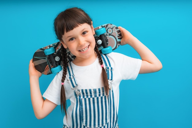 Funny child brunette girl  years old with a skate posing in isolation on a blue studio background