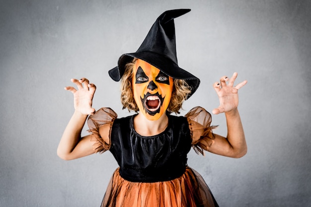 Смешной ребенок одетый костюм ведьмы. Малыш нарисовал ужасную тыкву. Концепция осеннего праздника хэллоуин