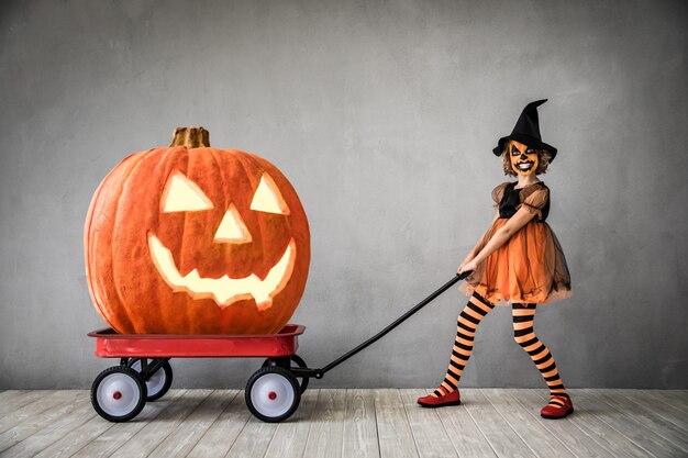 Funny child dressed witch costume. Kid painted terrible pumpkin. Halloween autumn holiday concept