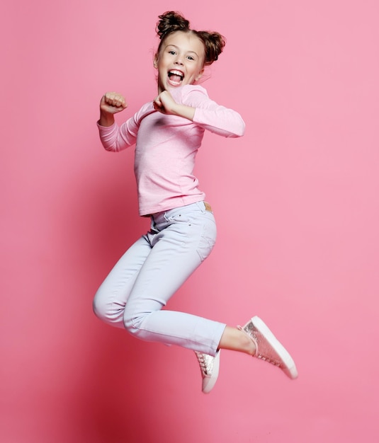 Funny child girl dressed casual jumping on pink background