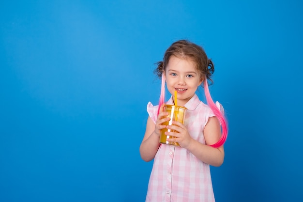 オレンジジュースのガラスを持って笑っているピンクの服を着た面白い子の女の子。