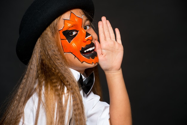 Funny child girl in pumpkin costume for Halloween. Halloween makeup. Face art.