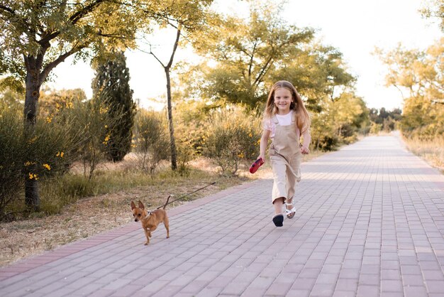 ペットの飼いならされた子犬の犬と一緒に公園で走っている面白い子の女の子