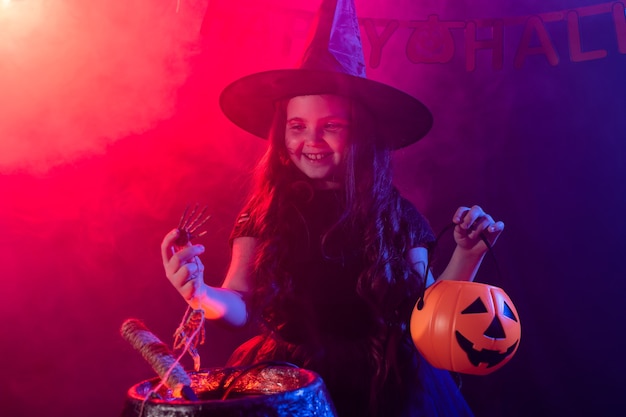 Funny child girl in witch costume for Halloween with pumpkin Jack.