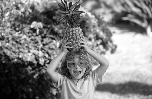 Funny child holds a pineapple on her head on a summer nature background pineapple kid boy and
