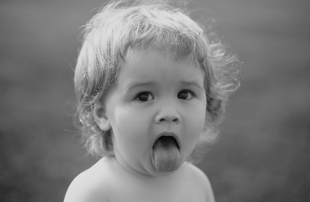 Funny child in park baby face with tongue close up funny little child closeup portrait blonde kid em
