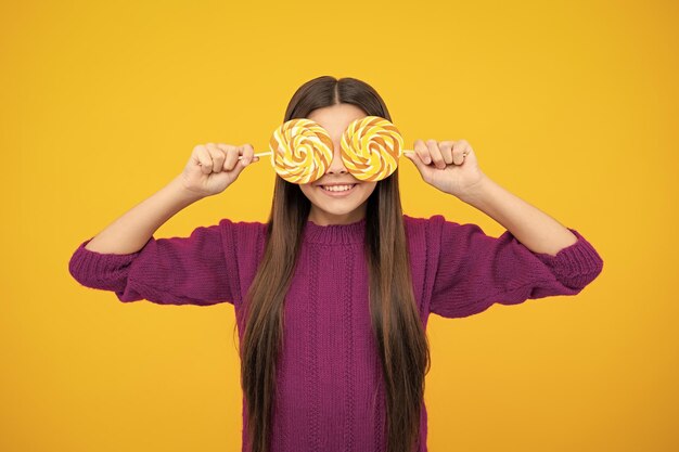 Funny child with lollipop over yellow isolated background sweet childhood life teen girl with yummy caramel lollipop candy shop teenager with sweet sucker