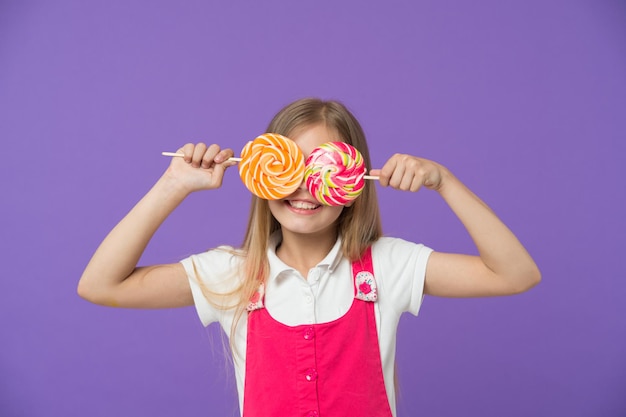 Funny child with lollipops on violet background Girl smiling with candy eyes Little kid smile with candies on sticks Sweet look Candyshop concept Childhood and happiness Having fun with candies