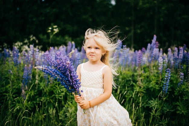 Funny child with offended face holding bouquet of blue flowers at nature in summer day.