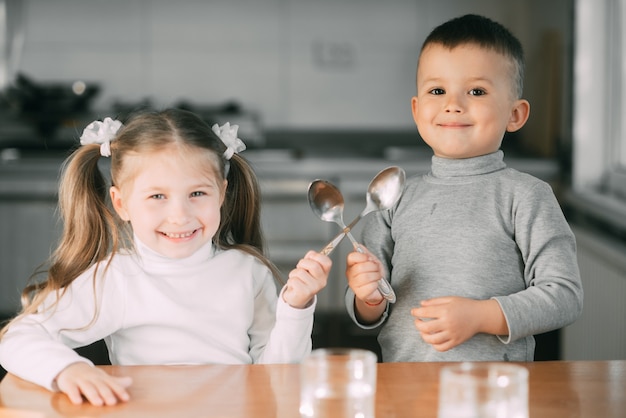 Funny children girl and boy in the kitchen with spoons, playing, going to eat cute