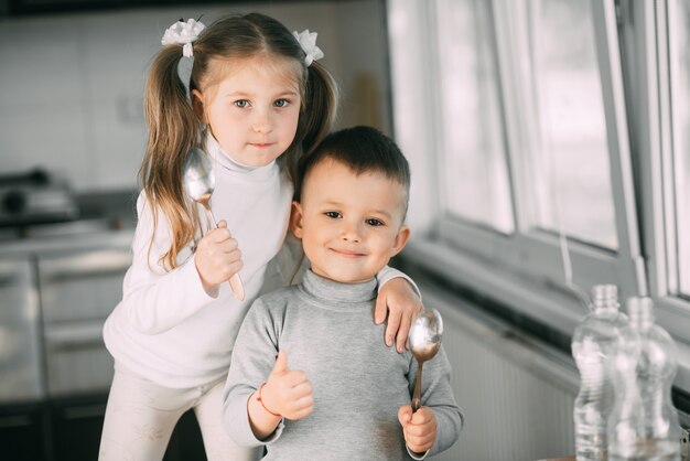 Funny children girl and boy in the kitchen with spoons, playing, going to eat cute