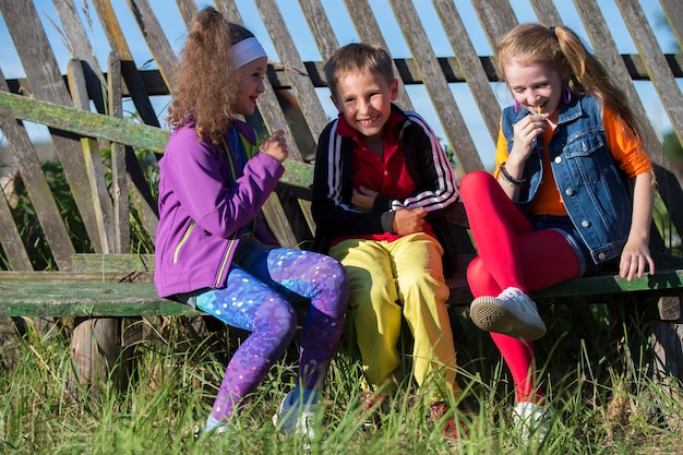 Funny children with bright make-up in krack clothes. A boy and two girls of school age are sitting on a wooden porch.