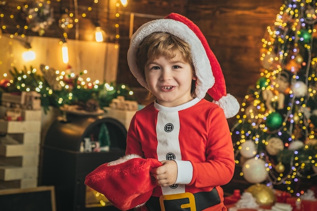 面白いクリスマスの子供たちは、クリスマスプレゼントの靴下で幸せな小さな笑顔の男の子に直面しています