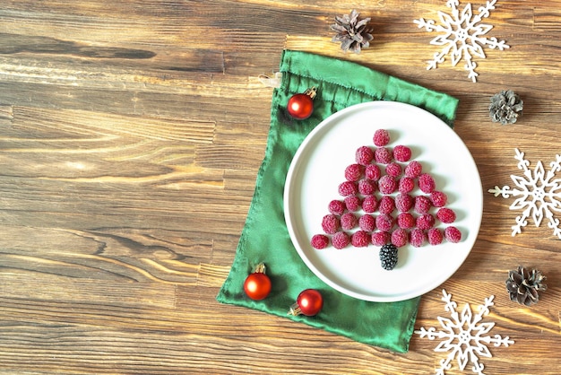 Funny Christmas tree shaped sweet fresh raspberry berry on plate on wooden background for kids children breakfast xmas food with new year decorations copy space